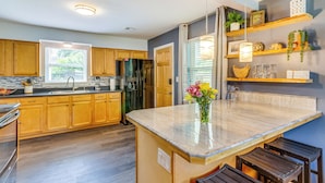 A modern kitchen with wooden cabinets, a central island, and built-in shelves. - Pet-friendly Pensacola Home w/ Sunny Backyard! (Pensacola)