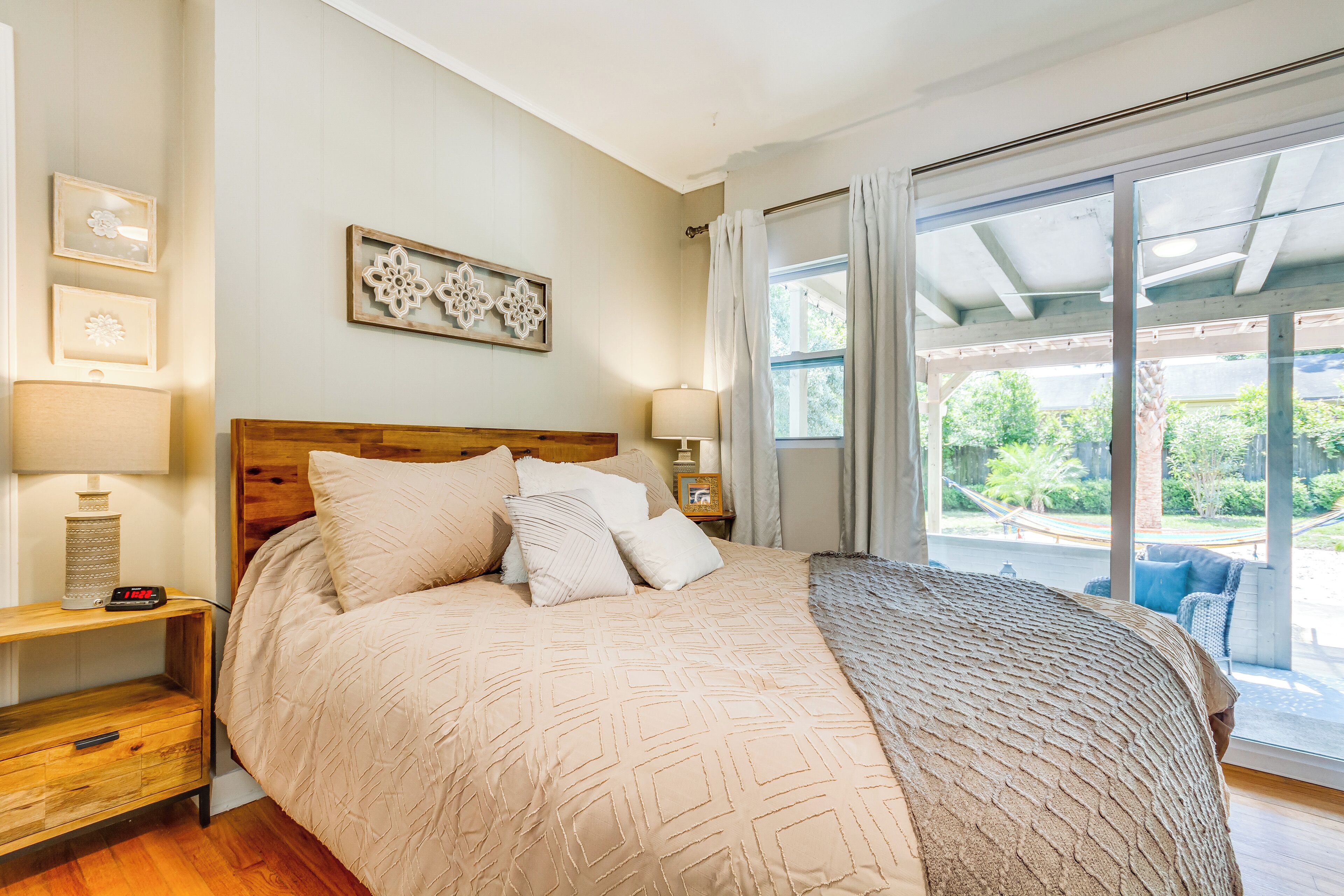 Une chambre à coucher avec une tête de lit en bois, un grand lit recouvert d’une literie à motifs, une table de chevet avec une lampe, et une vue sur l’extérieur grâce à une porte-fenêtre coulissante.
