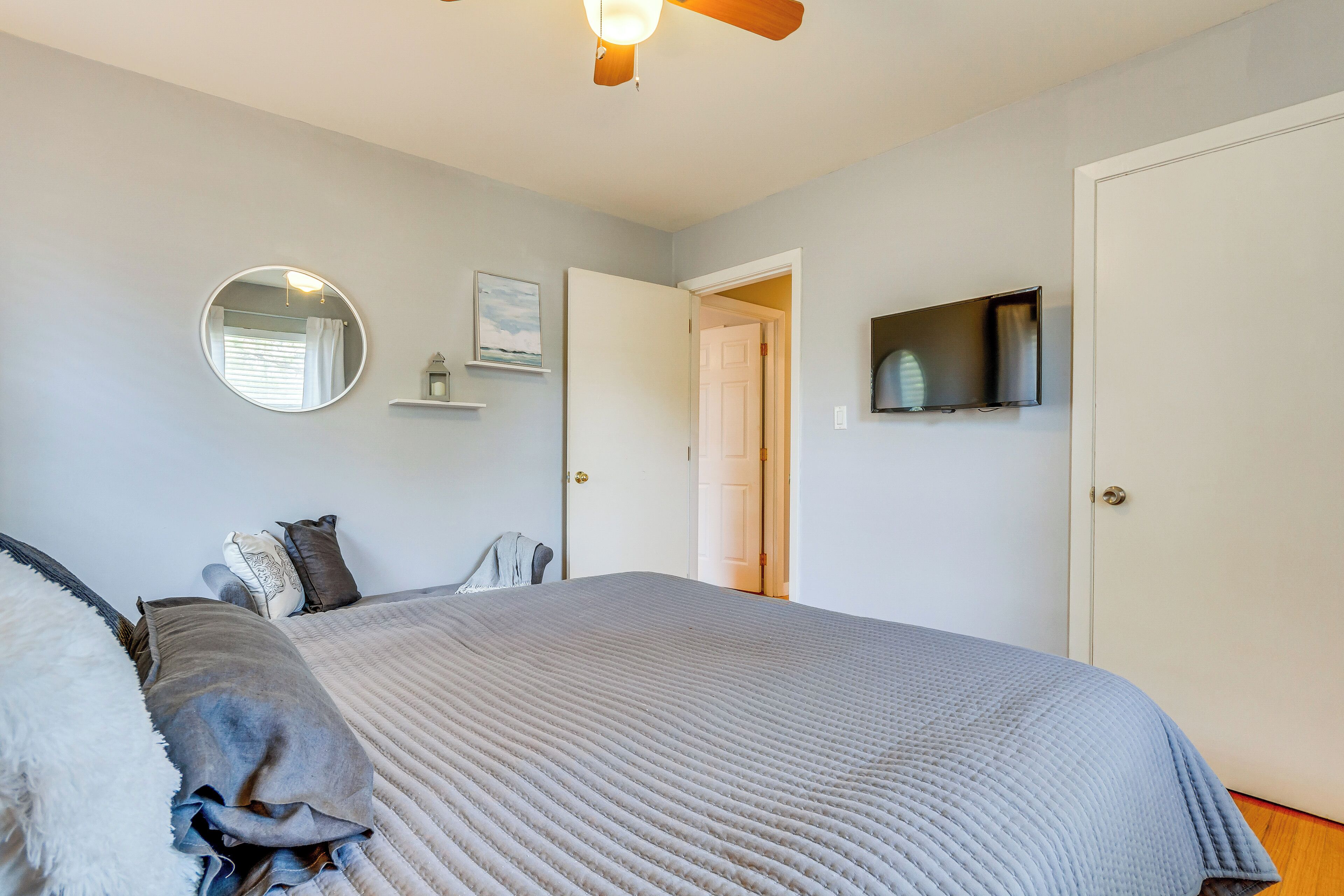 A bedroom with a bed, a ceiling fan, a TV mounted on the wall, and a door leading to another room.