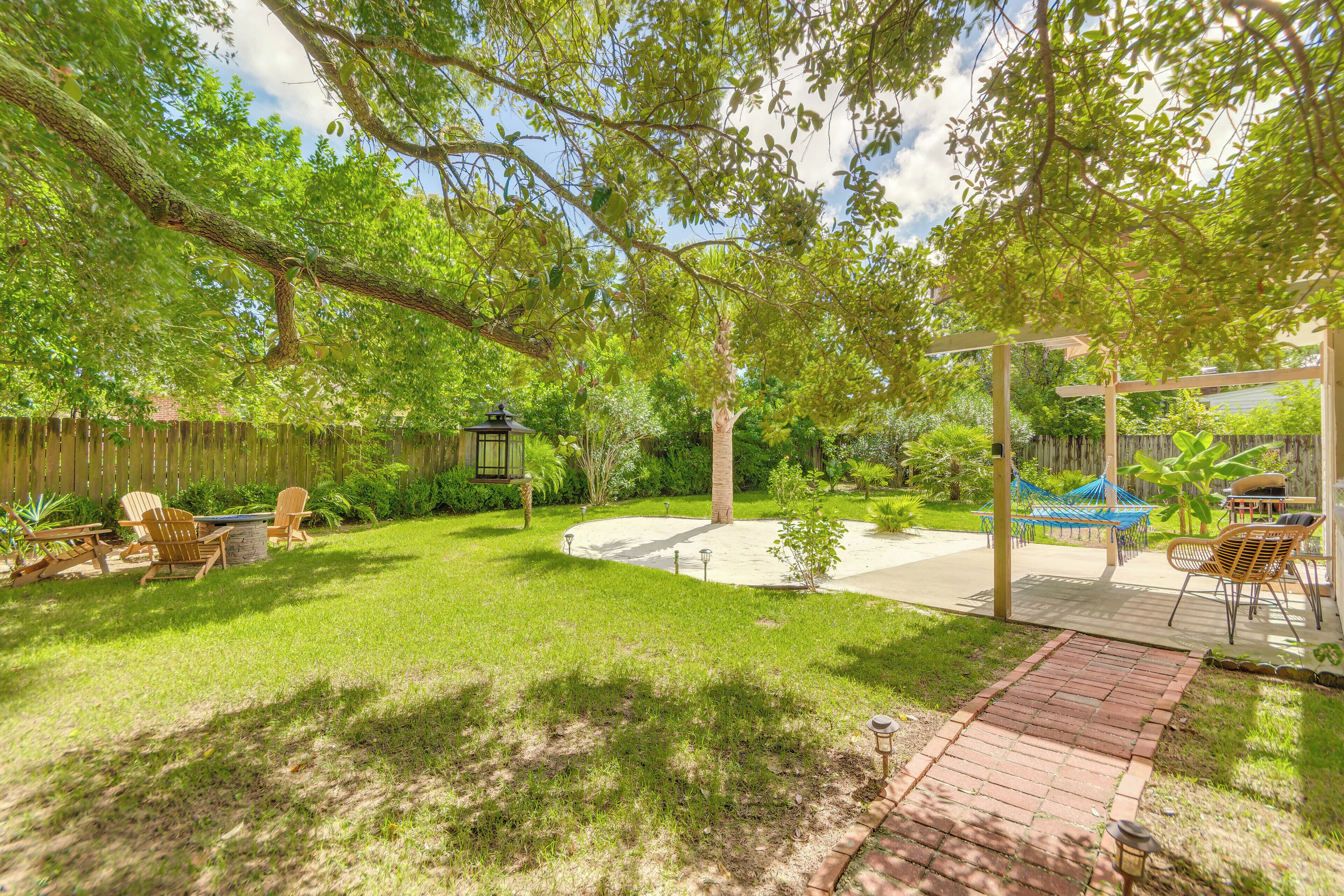 Un jardin avec une terrasse, des chaises, un hamac et une clôture en bois.