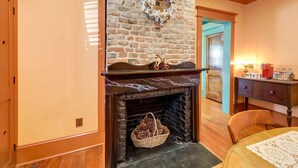 A cozy room with a brick fireplace, a wicker basket, and a wooden table. - Victorian Vacation Rental Apt in Downtown New Bern (New Bern)