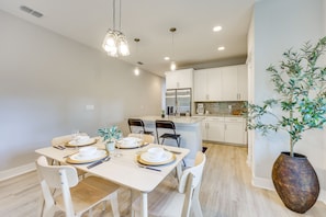 A modern kitchen with white cabinets, a stainless steel refrigerator, and a dining area with a wooden table and chairs. - New-build Jacksonville Townhome w/ Private Yard! (Jacksonville)