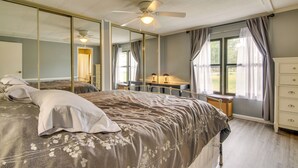 Une chambre à coucher avec un grand lit, un bureau et une chaise, un ventilateur de plafond et une grande fenêtre avec des rideaux.