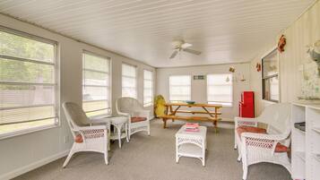Una habitación con muebles de mimbre blanco, ventilador de techo y una mesa de picnic.
