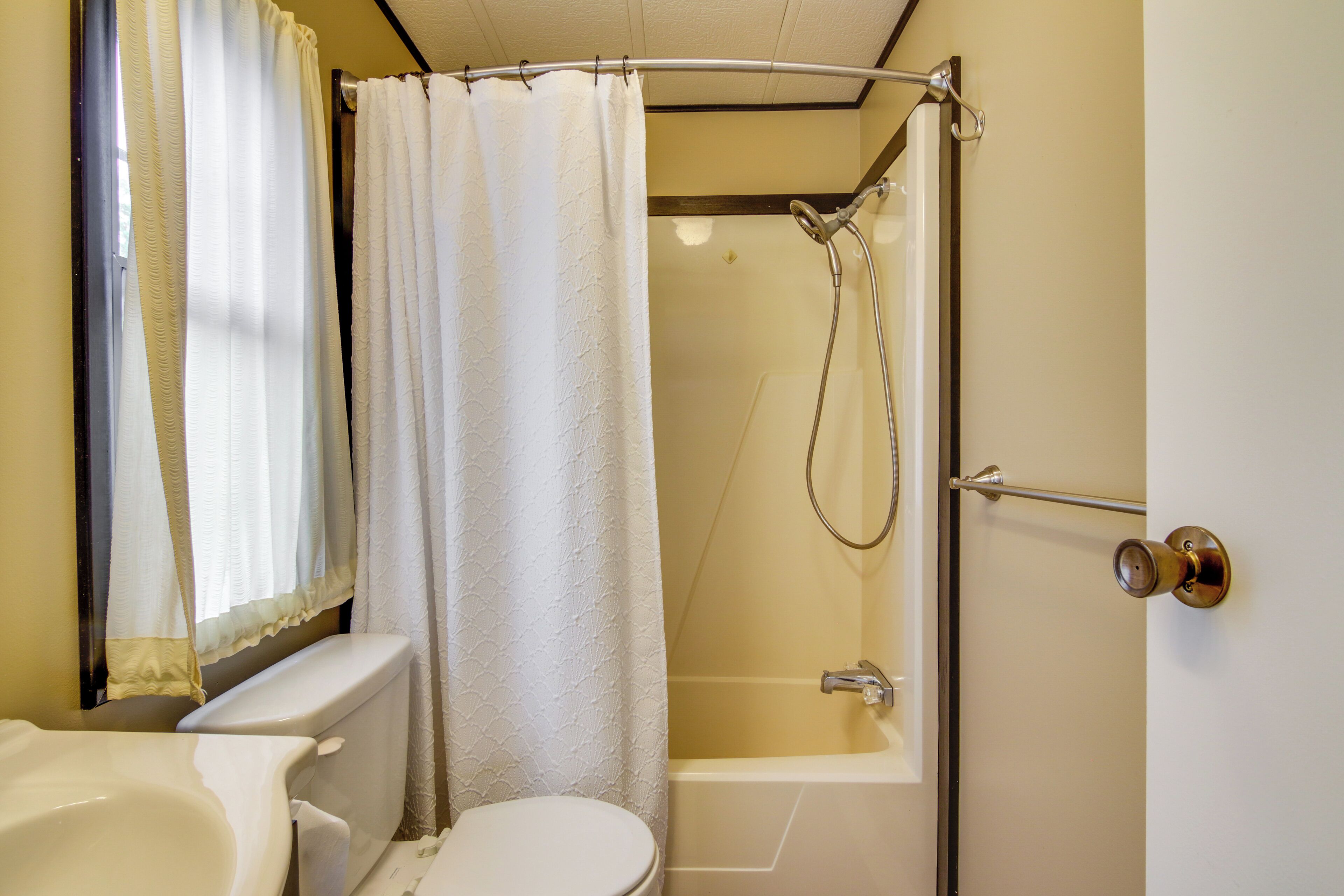 A bathroom with a toilet, sink, shower, and a door with a towel rack.
