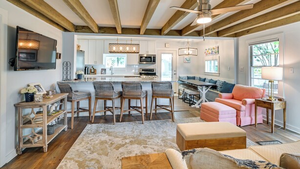 A spacious living area with a kitchen, wooden beams, a ceiling fan, and a large window. - Chic Historic Myrtle Beach Cottage: Steps to Beach (Myrtle Beach)
