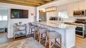 A modern kitchen with white cabinets, stainless steel appliances, and a large island with bar stools. - Chic Historic Myrtle Beach Cottage: Steps to Beach (Myrtle Beach)
