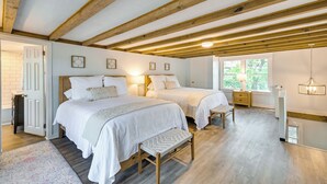 A bedroom with two beds, wooden beams, a window with a view, and a bedside table with a lamp. - Chic Historic Myrtle Beach Cottage: Steps to Beach (Myrtle Beach)