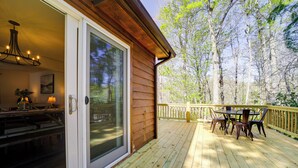 A wooden deck with a dining area and a sliding glass door leading to an interior space with a chandelier. - Peaceful Candler Cabin w/ Private Hot Tub! (Candler)