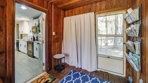 A wooden interior with a kitchen, a small stool, a window with curtains, and a shelf with mail. - Peaceful Candler Cabin w/ Private Hot Tub! (Candler)