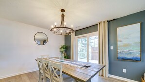 A dining area with a wooden table, white chairs, a chandelier, a round mirror, and a large painting on the wall. - Peaceful Candler Cabin w/ Private Hot Tub! (Candler)