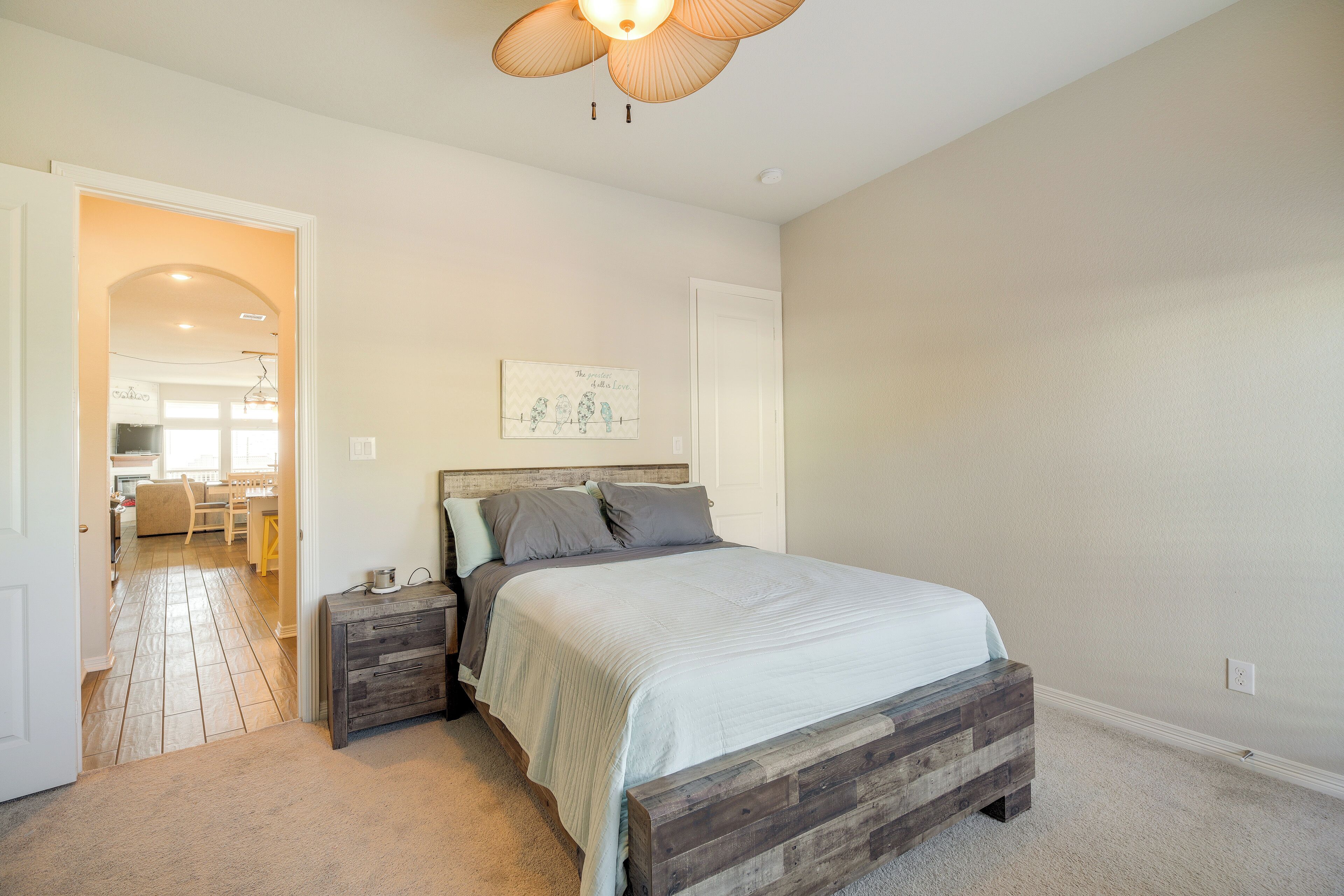 A bedroom with a wooden bed, a nightstand, a wall-mounted artwork, and a hallway leading to a dining area.