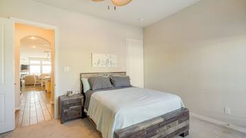 A bedroom with a wooden bed, a nightstand, a wall-mounted artwork, and a hallway leading to a dining area.