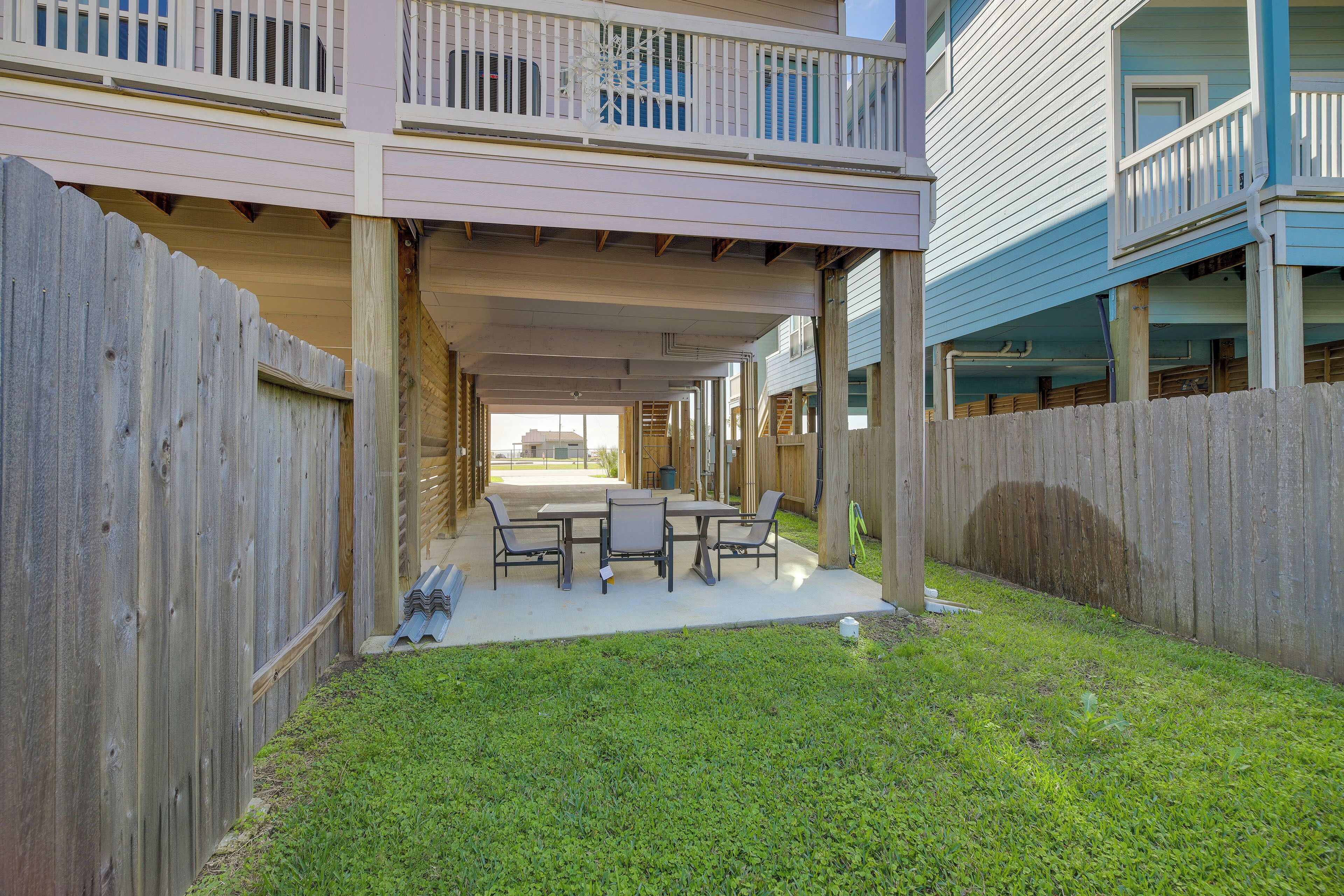 A covered patio with a table and chairs, a wooden fence, and a grassy area.