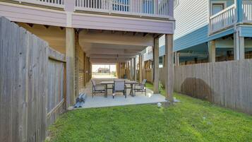 A covered patio with a table and chairs, a wooden fence, and a grassy area.