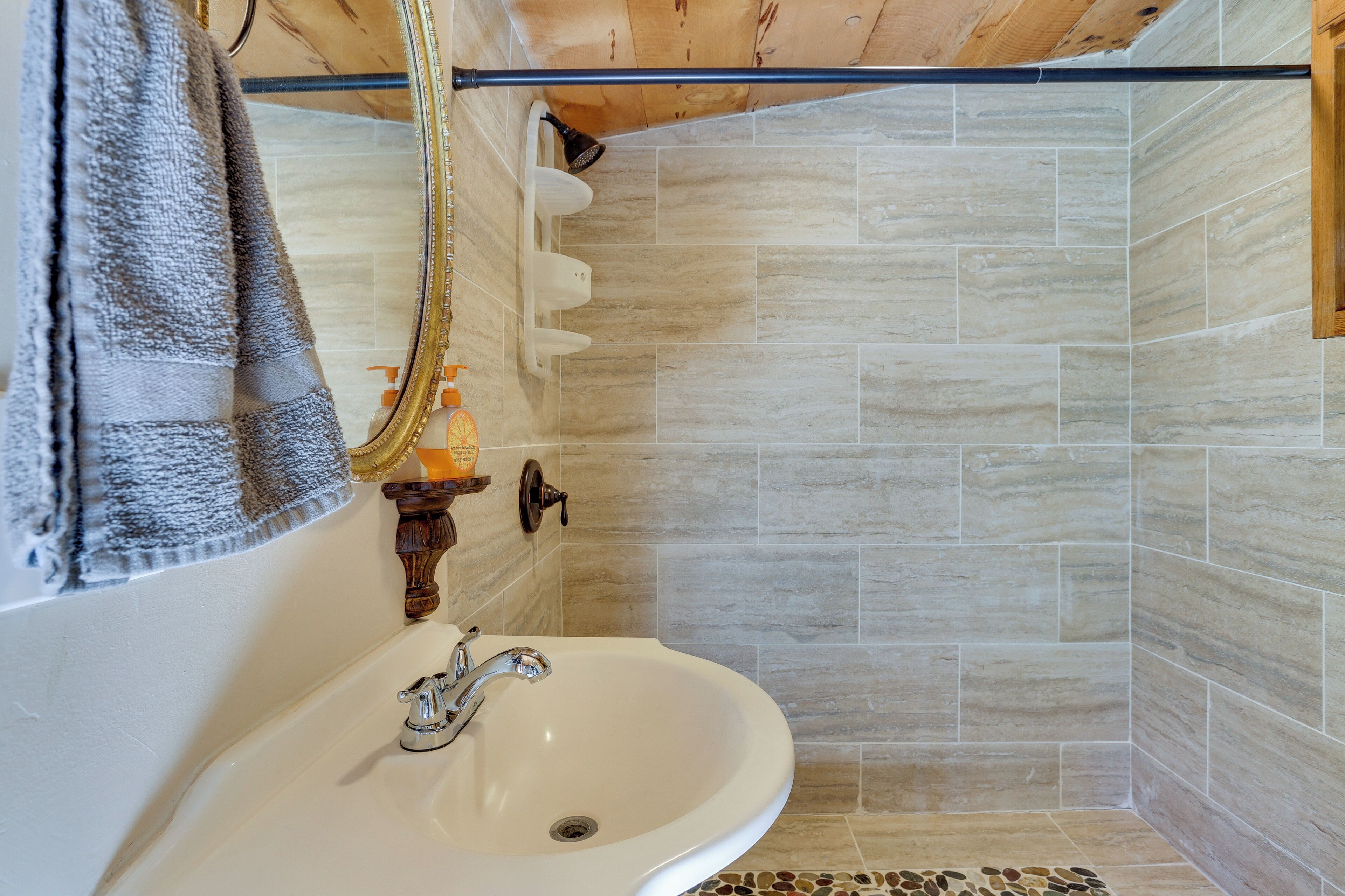 Ein Badezimmer mit einem weißen Waschbecken, einer Dusche mit beigen Fliesen und einer Holzboden.