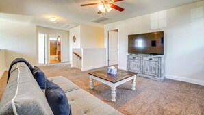 Ein Wohnzimmer mit Deckenventilator, Fernseher und Couchtisch aus Holz.
