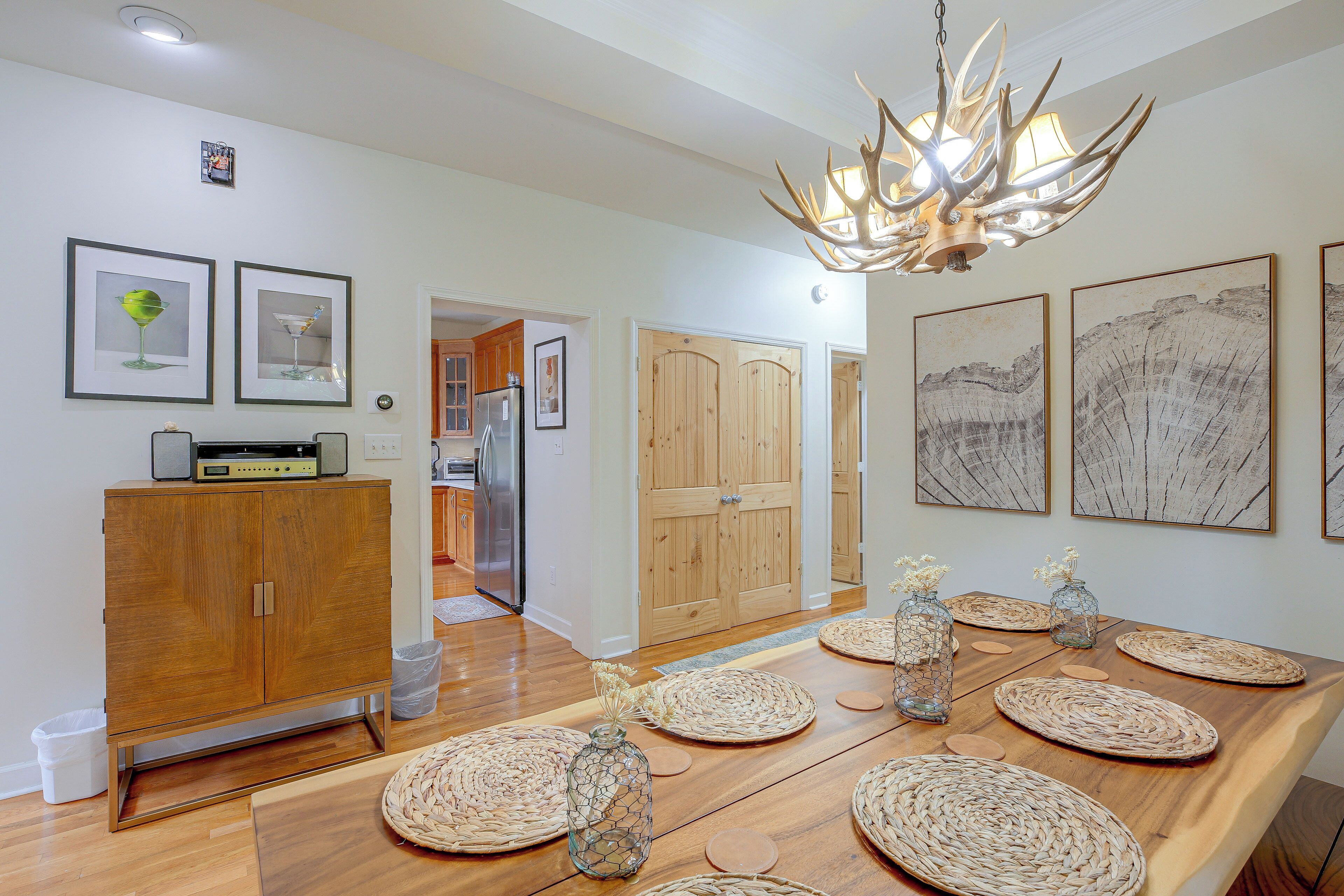A modern kitchen with wooden cabinets, a stainless steel refrigerator, and a dining table set with woven placemats and glass vases.