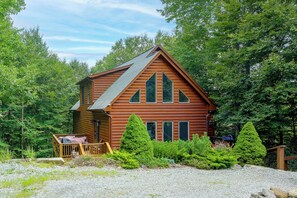 A log cabin with a porch, surrounded by dense greenery.