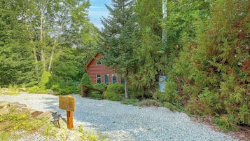 A cabin surrounded by dense forest with a gravel path leading to it.