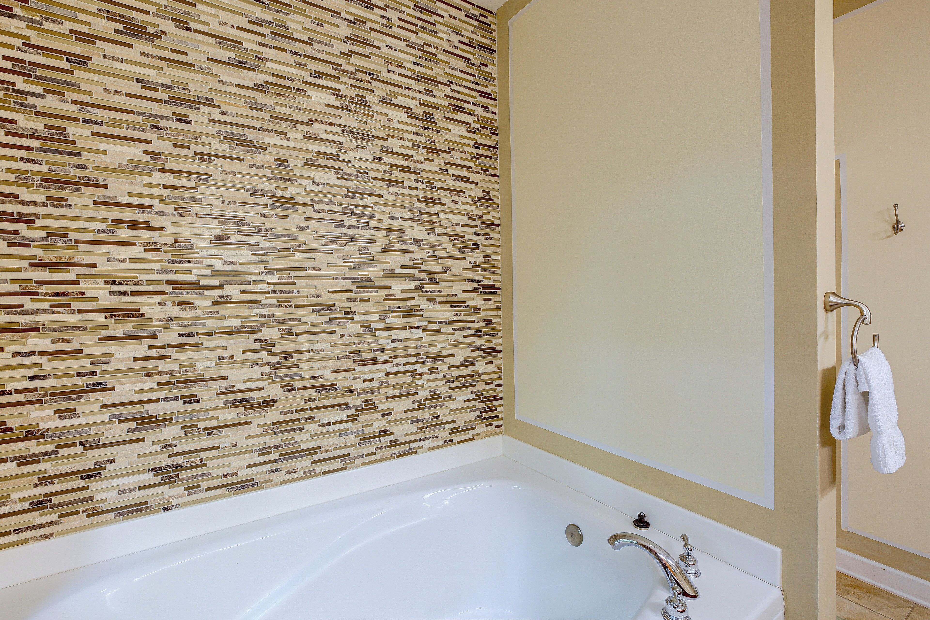 A bathroom with a tiled wall, a bathtub, and a towel rack.
