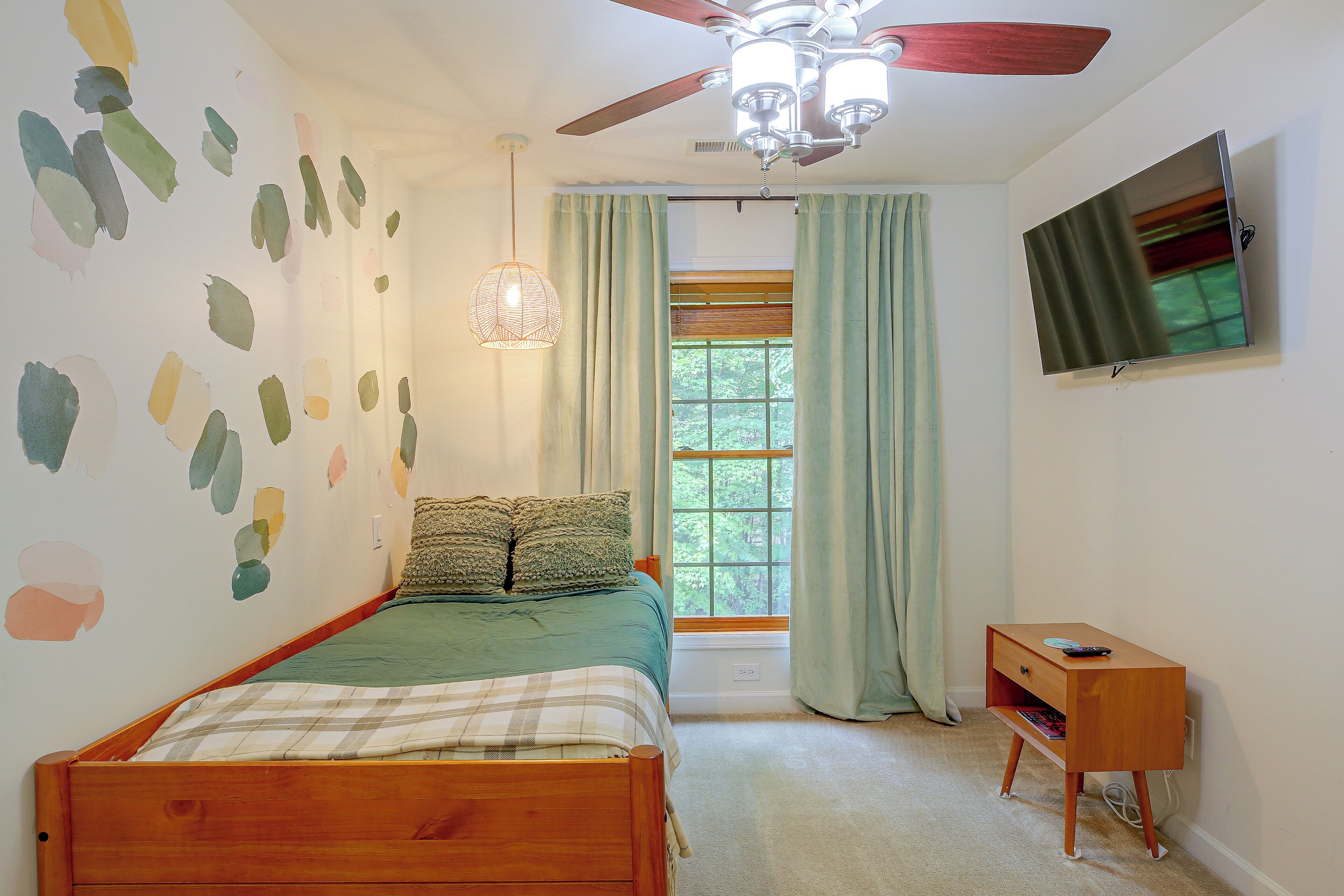Una camera da letto con un letto di legno, una ventola a soffitto, una finestra con tende e un televisore a parete.