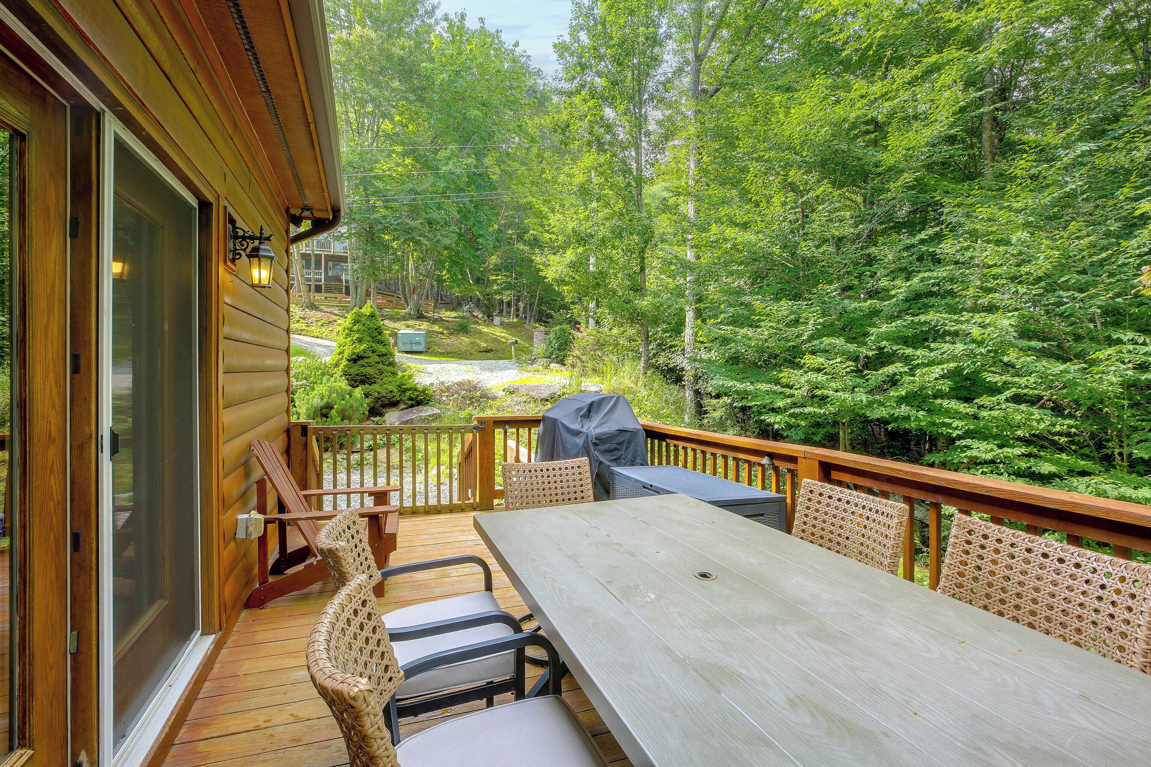 A wooden deck with a table and chairs, overlooking a forested area.