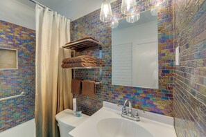 A bathroom with a tiled mosaic wall, a white sink, a mirror, a towel rack, and a shower curtain. - Charming New Bern Cottage w/ Grill & Fire Pit! (New Bern)