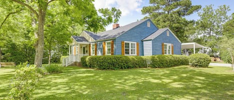 A two-story house with a well-maintained lawn, a covered porch, and a large tree in the foreground.