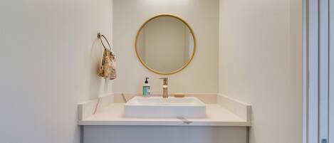 A bathroom with a white sink, a round mirror, a handheld soap dispenser, and a small towel hanging on the wall.