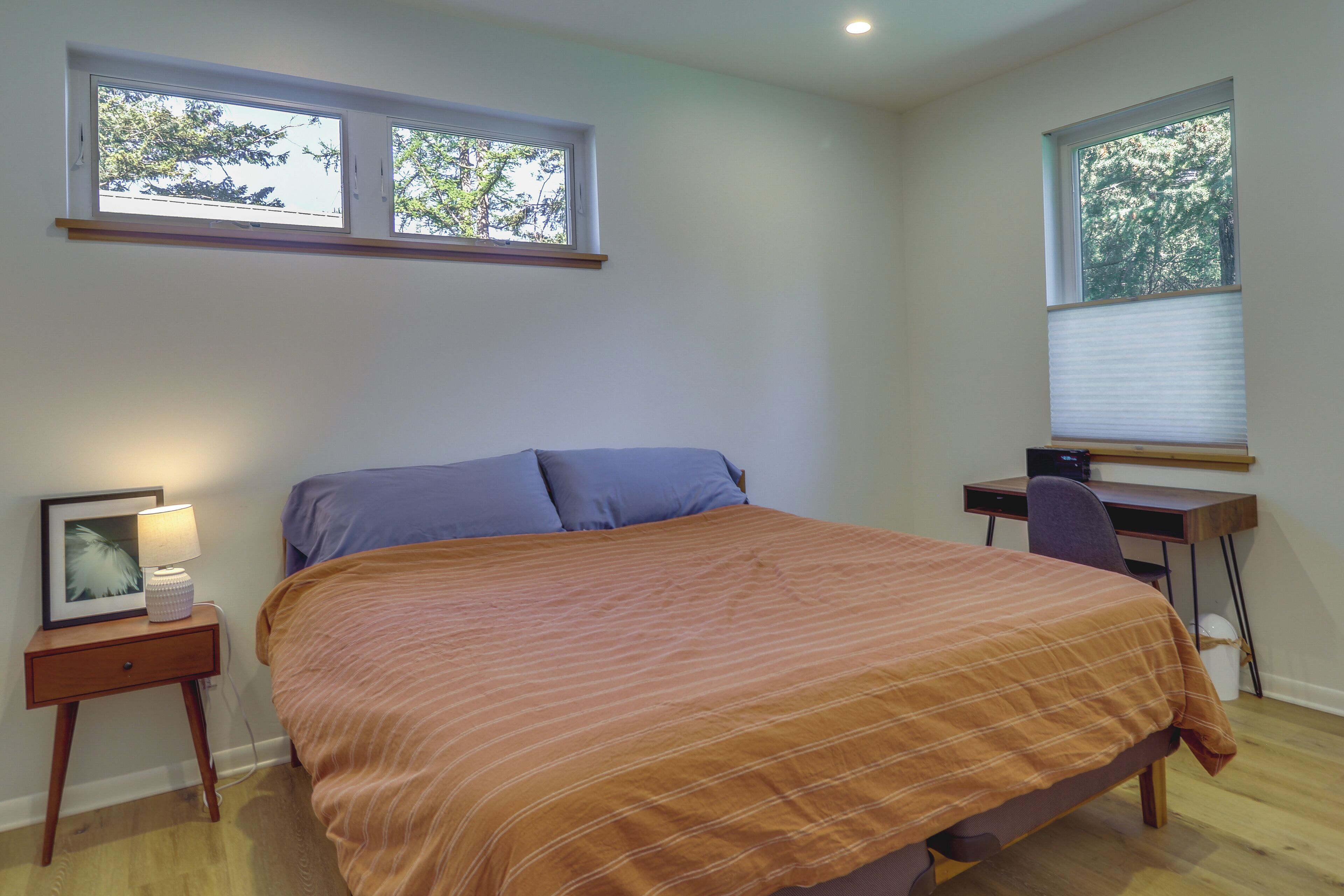 A bedroom with a bed, a desk, and two windows.