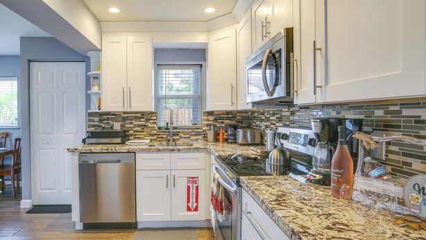 A modern kitchen with white cabinets, a stainless steel dishwasher, a microwave, and a granite countertop. - Private Pool & Patio: Fort Lauderdale Home! (Fort Lauderdale)