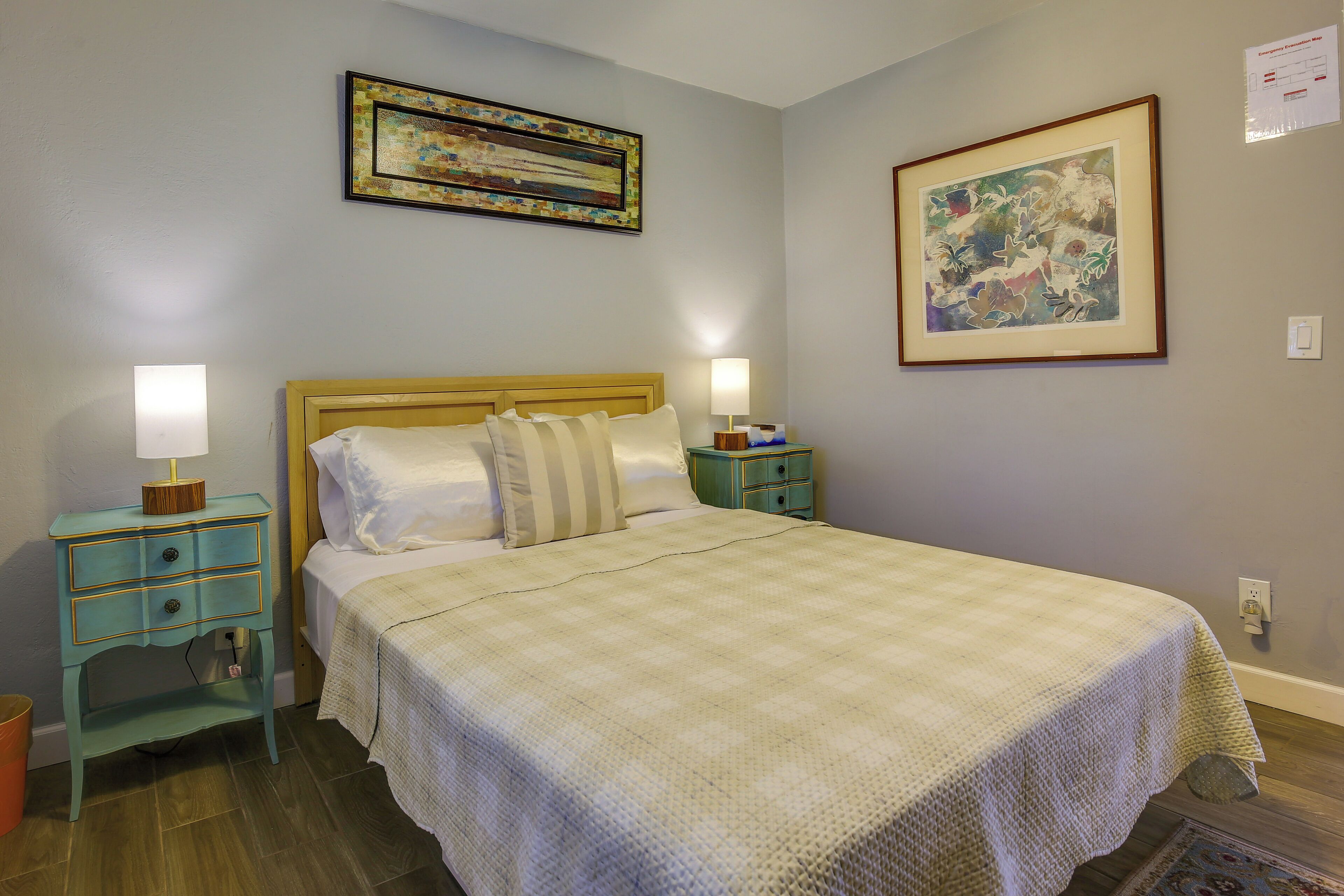 A bedroom with a bed, two bedside tables, a nightstand, a lamp, and two framed pictures on the wall.
