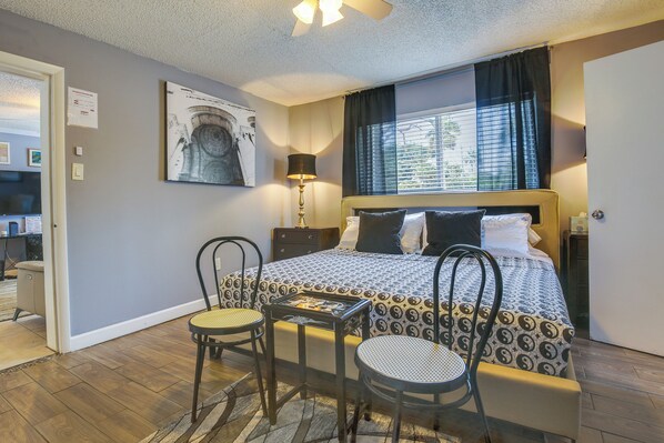 A hotel room with a bed, two chairs, a table with a board game, a lamp, and a window with curtains.