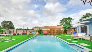 A swimming pool with a wooden deck, red and blue lounge chairs, and a small table. - Private Pool & Patio: Fort Lauderdale Home! (Fort Lauderdale)