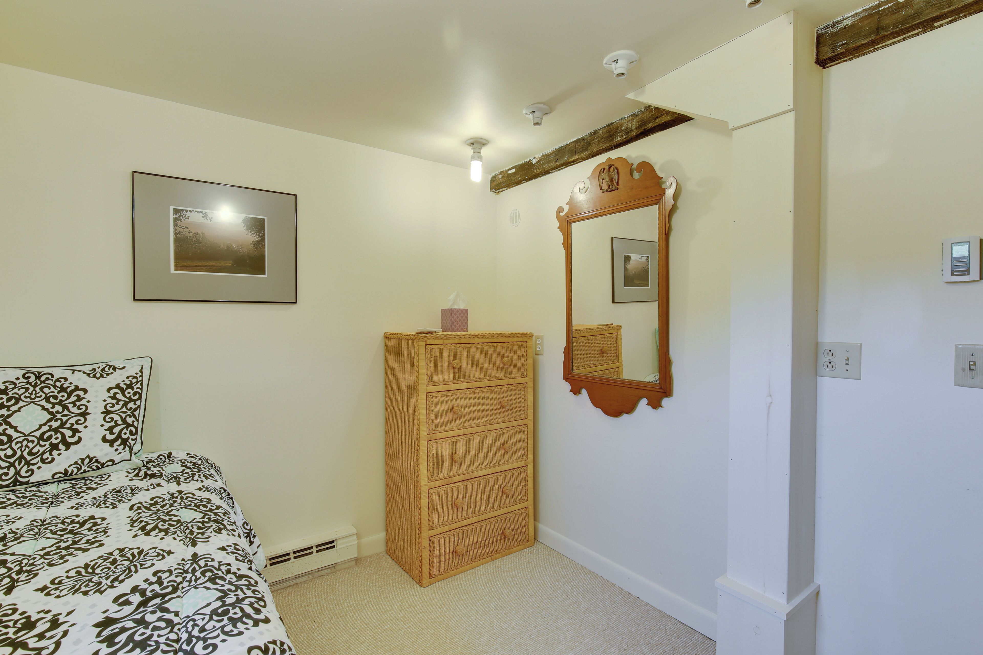 A bedroom with a bed, a wooden dresser, a mirror, and a framed picture on the wall.