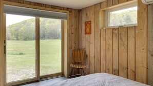 A bedroom with a large sliding glass door, a wooden chair, and a small window. - Serene Salisbury Rental Home on 26 Acres w/ Deck! (Falls Village)