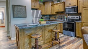 A kitchen with wooden cabinets, stainless steel appliances, and a central island with stools. - Raymondville Apartment w/ Patio: Near Lakes! (Raymondville)