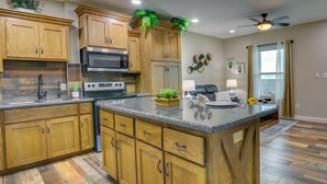A kitchen with wooden cabinets, a granite countertop, a microwave, and a ceiling fan. - Raymondville Apartment w/ Patio: Near Lakes! (Raymondville)