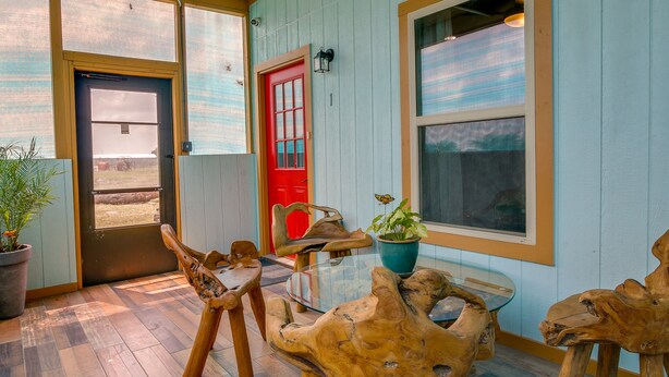 A wooden dining table with chairs, a red door, and a window with a view. - Raymondville Apartment w/ Patio: Near Lakes! (Raymondville)