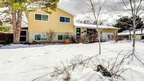 Una casa de dos pisos con fachada amarilla, un garaje y un jardín delantero cubierto de nieve.