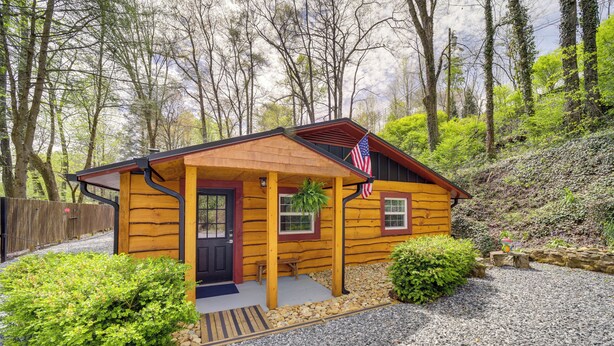 A small log cabin with a porch, a front door, and an American flag. - Multi-unit Brevard Vacation Rental With Patio! (Brevard)