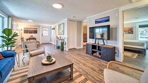A modern living room with a sofa, coffee table, and TV. There is a dining area with a table and chairs, and a kitchen area with cabinets and a countertop. - Multi-unit Brevard Vacation Rental With Patio! (Brevard)