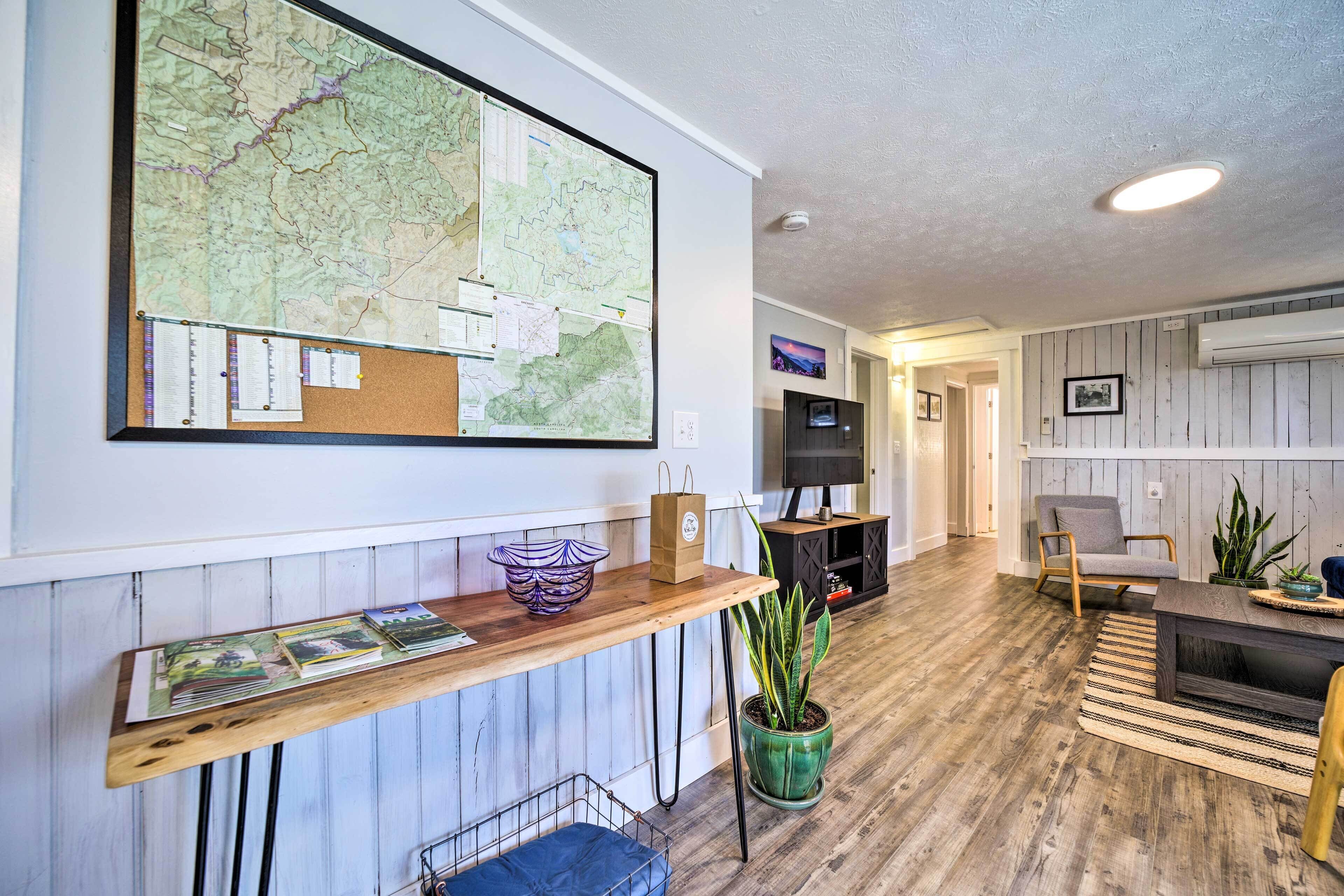 A living room with a large map on the wall, a wooden coffee table, a green potted plant, a TV, and a seating area with a chair and sofa.