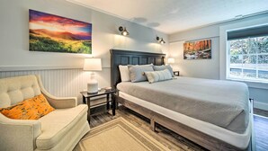 A bedroom with a large bed, a nightstand, a chair, and two wall-mounted lamps. - Multi-unit Brevard Vacation Rental With Patio! (Brevard)