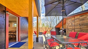 An outdoor patio with a glass table and red chairs, a wooden deck, and a brick wall. - Multi-unit Brevard Vacation Rental With Patio! (Brevard)
