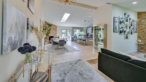 A spacious living area with a dining table, a sofa, and a chandelier. There are abstract paintings on the walls and a kitchen in the background. - California Getaway w/ Private Outdoor Pool (Escondido)