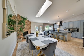 A modern kitchen with grey cabinets, a central island, and a dining area with a white table and grey chairs. - California Getaway w/ Private Outdoor Pool (Escondido)