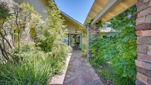 A stone pathway leading to a building entrance, surrounded by lush greenery and a stone wall. - California Getaway w/ Private Outdoor Pool (Escondido)