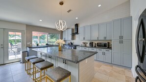 A modern kitchen with grey cabinets, a large island with bar stools, a built-in microwave, and a stainless steel refrigerator. - California Getaway w/ Private Outdoor Pool (Escondido)